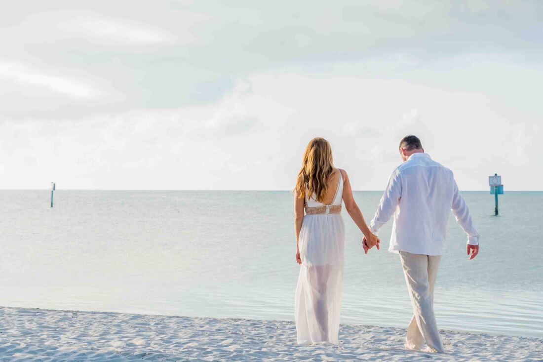 A couple walking along the beach holding hands, while a key west wedding photographer captures their joy.