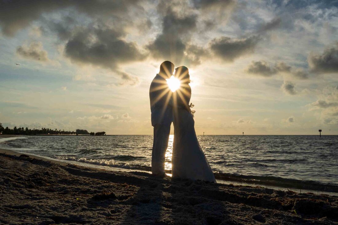 A couple - bride and groom - share a romantic kiss on the beach at sunset, captured beautifully by a talented Key West wedding photographer.