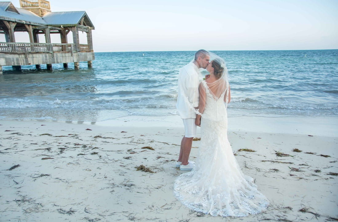 A bride and groom exchanging vows on the beach near a pier, captured beautifully by a skilled Key West wedding photographer.