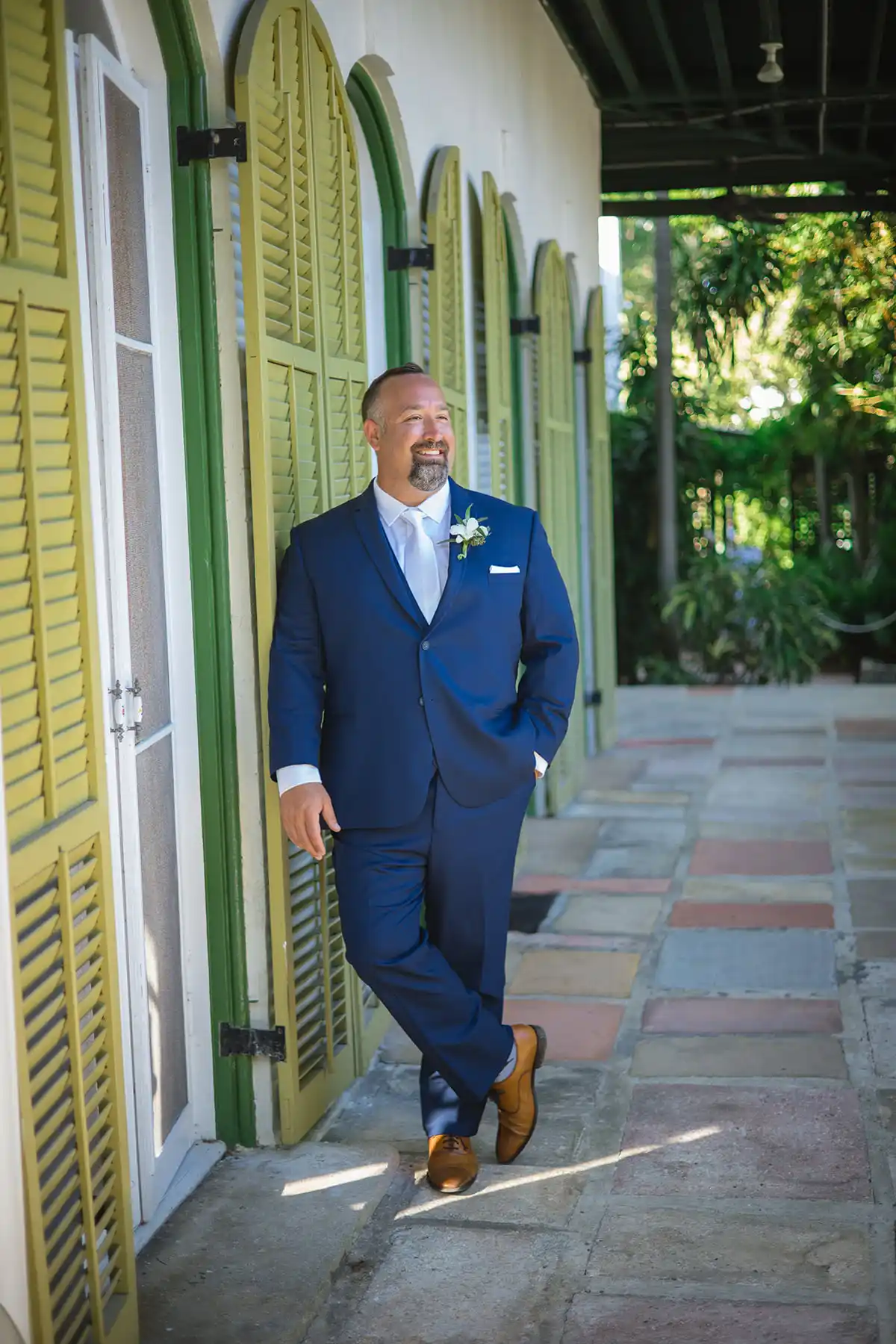 A groom in a blue suit standing in front of some green shutters, captured beautifully by a key west wedding photographer.