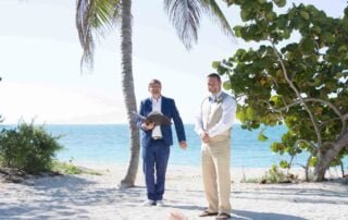 Two men standing on the beach with palm trees in the background, capturing a beautiful moment from their Key West wedding.