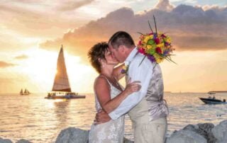 A bride and groom share a romantic kiss in front of a sailboat at sunset, captured by a skilled Key West wedding photographer.