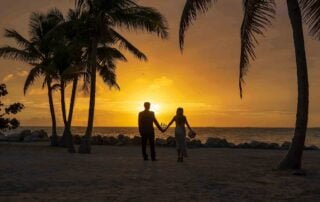 A couple holding hands on the beach at sunset during their romantic Key West wedding.