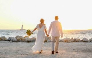 A stunning bride and handsome groom walk hand in hand on a picturesque beach at sunset, captured beautifully by a talented Key West wedding photographer.