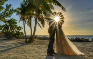 A bride and groom kiss in front of palm trees on the beach, celebrating their idyllic Key West wedding.