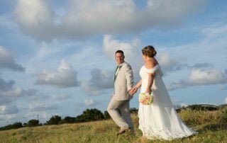 A bride and groom, captured by a talented Key West wedding photographer, walking hand in hand through a picturesque grassy field during their beautifully arranged Key West wedding.
