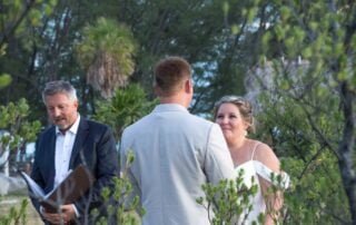 A bride and groom, captured by a skilled Key West wedding photographer, exchange heartfelt vows in front of lush bushes during their dreamy Key West wedding.
