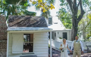 A key west wedding photographer captures a bride and groom walking in front of a white house during their beautiful key west wedding.