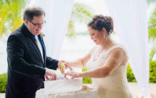 A couple celebrating their special day in Key West, with the help of a skilled wedding planner and officiant, joyfully cutting their wedding cake together.