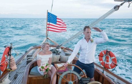 An enchanting key west wedding ceremony takes place on a boat, where a beaming bride and groom exchange vows against the backdrop of a fluttering American flag.