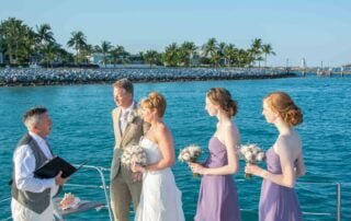A group of bridesmaids and groom stand on the deck of a boat during a scenic Key West wedding.