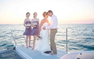 A bride and her bridesmaids, captured by a talented Key West wedding photographer, share a joyful moment as they embrace and kiss on the bow of a boat during their picturesque Key West wedding ceremony