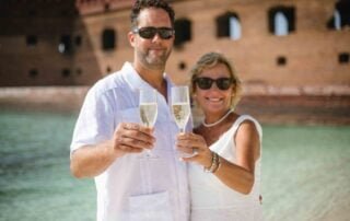 A couple holding champagne glasses on the beach, celebrating their Key West wedding.