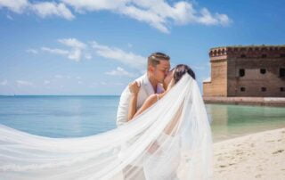 A bride and groom kissing on the beach at Fort McDowell captured by a Key West wedding photographer.