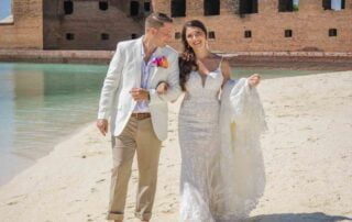 A bride and groom standing on the beach for their dream Key West wedding, with an old fort creating a picturesque backdrop.