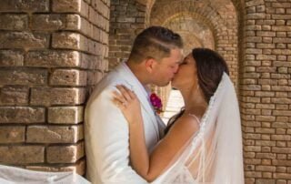 A bride and groom share a passionate kiss in front of a beautifully decorated archway at their Key West wedding ceremony.