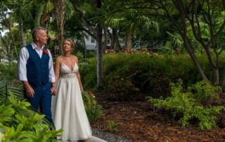 A bride and groom are gracefully walking down a path in a garden, captured beautifully by a key west wedding photographer.