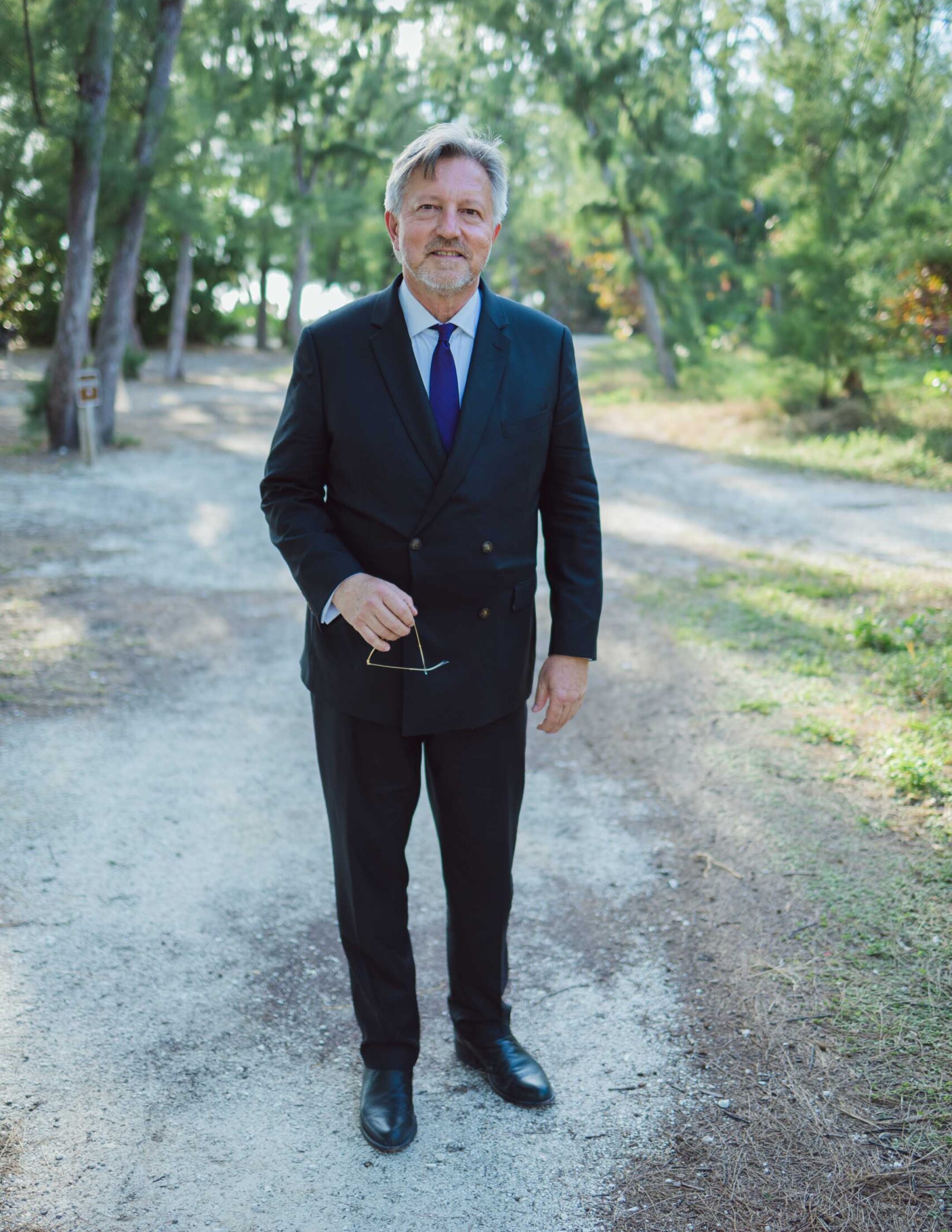 Michael Vernon A man in a suit standing on a dirt road, surrounded by the serene beauty of Key West.
